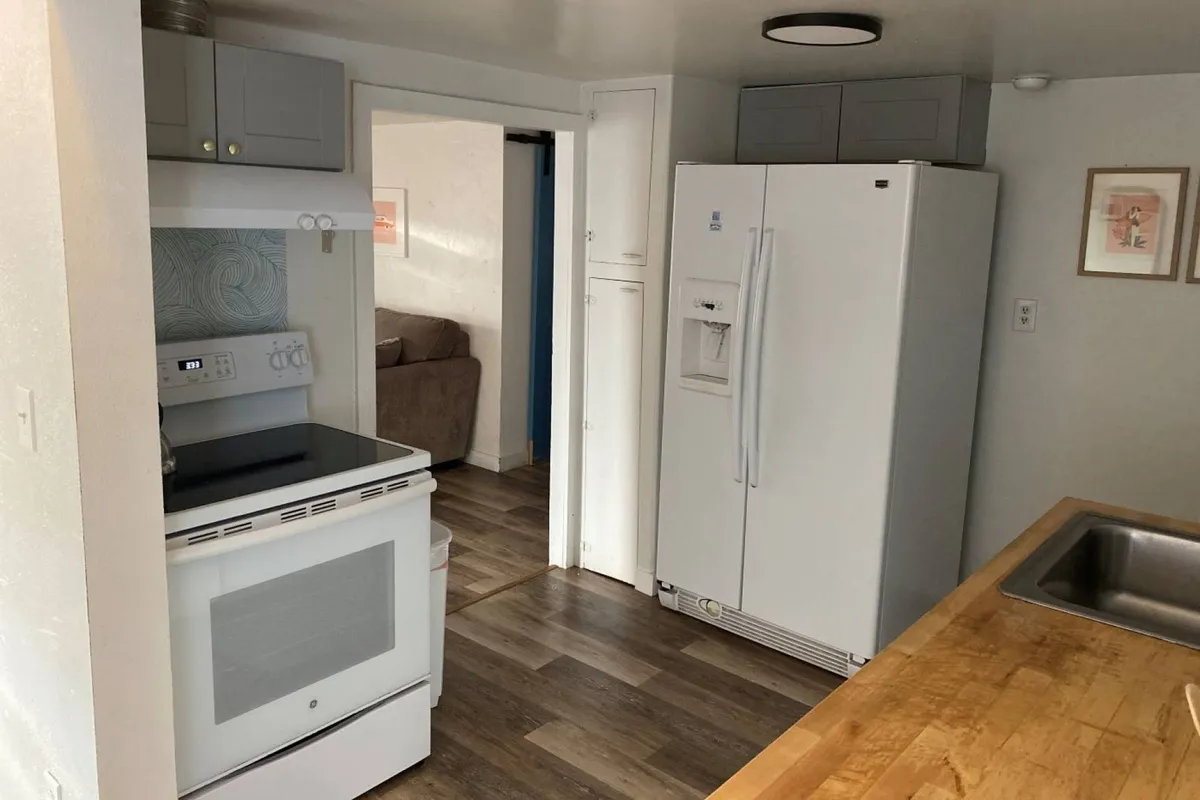 A comfortable kitchen scene with wooden countertops and visible kitchen appliances, this image offers a glimpse through an open doorway into the adjacent living area, hinting at the seamless flow between the spaces. The setup suggests a place for both cooking and gathering, reinforcing the open-concept theme.
