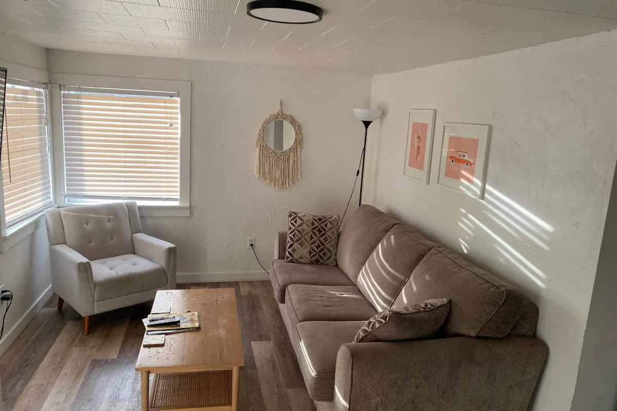 The image showcases a bright, inviting living area with a plush sofa and armchair arranged around a cozy coffee table, accented by thoughtful wall art and a glowing lamp, creating a warm, welcoming atmosphere perfect for relaxation or socializing.